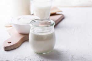 Unlabeled glass of yogurt in the foreground with a ceramic bowl of yogurt and a glass of milk in the background, highlighting UV decontamination of dairy products, packaging, surfaces, air and water.